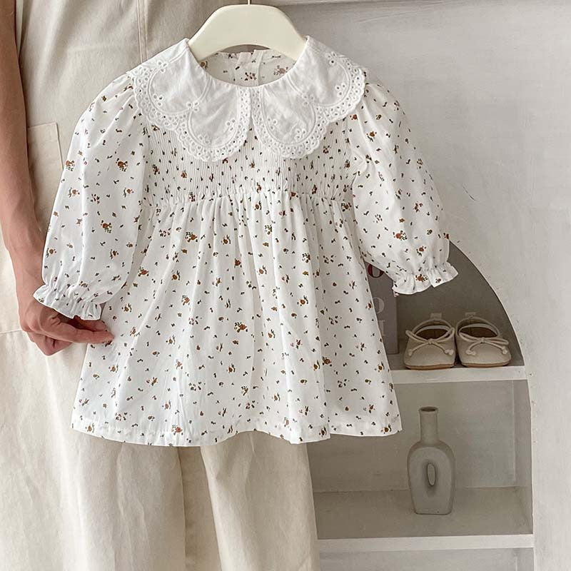 Baby girl wearing a floral pattern doll neck onesie and dress in white and beige, showcasing a cute and stylish design.