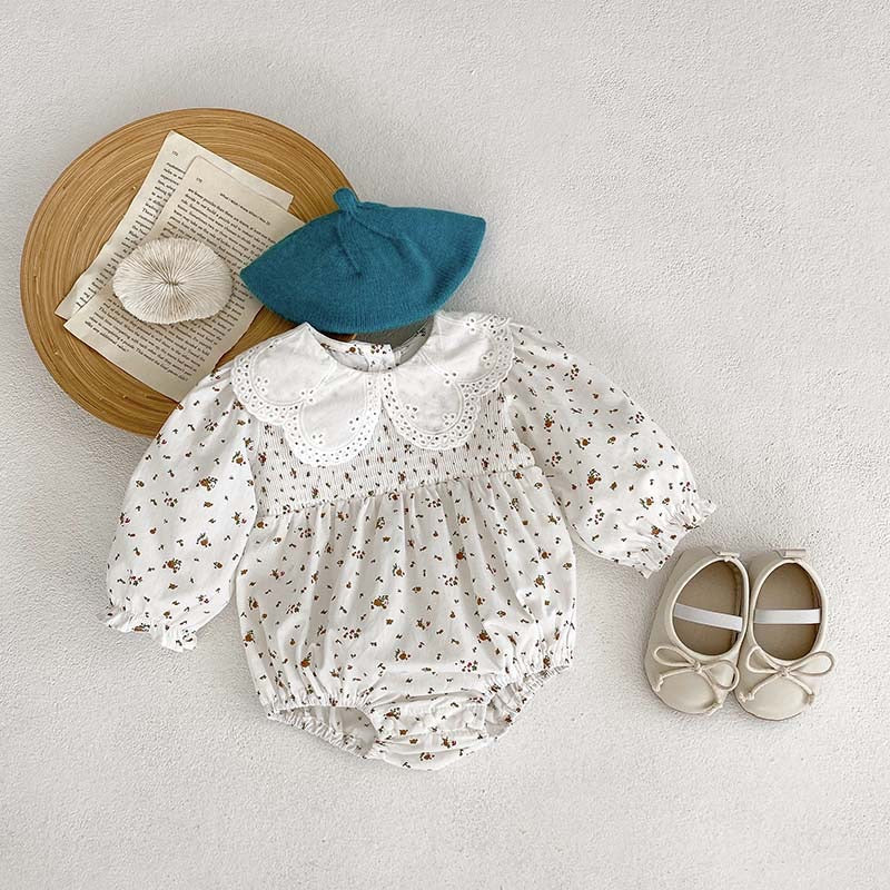 Baby girl wearing a floral pattern doll neck onesie and dress in white and beige, showcasing a cute and stylish design.