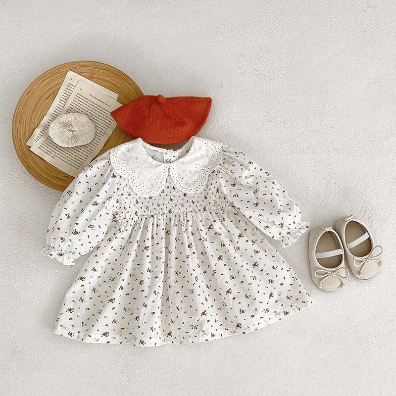 Baby girl wearing a floral pattern doll neck onesie and dress in white and beige, showcasing a cute and stylish design.