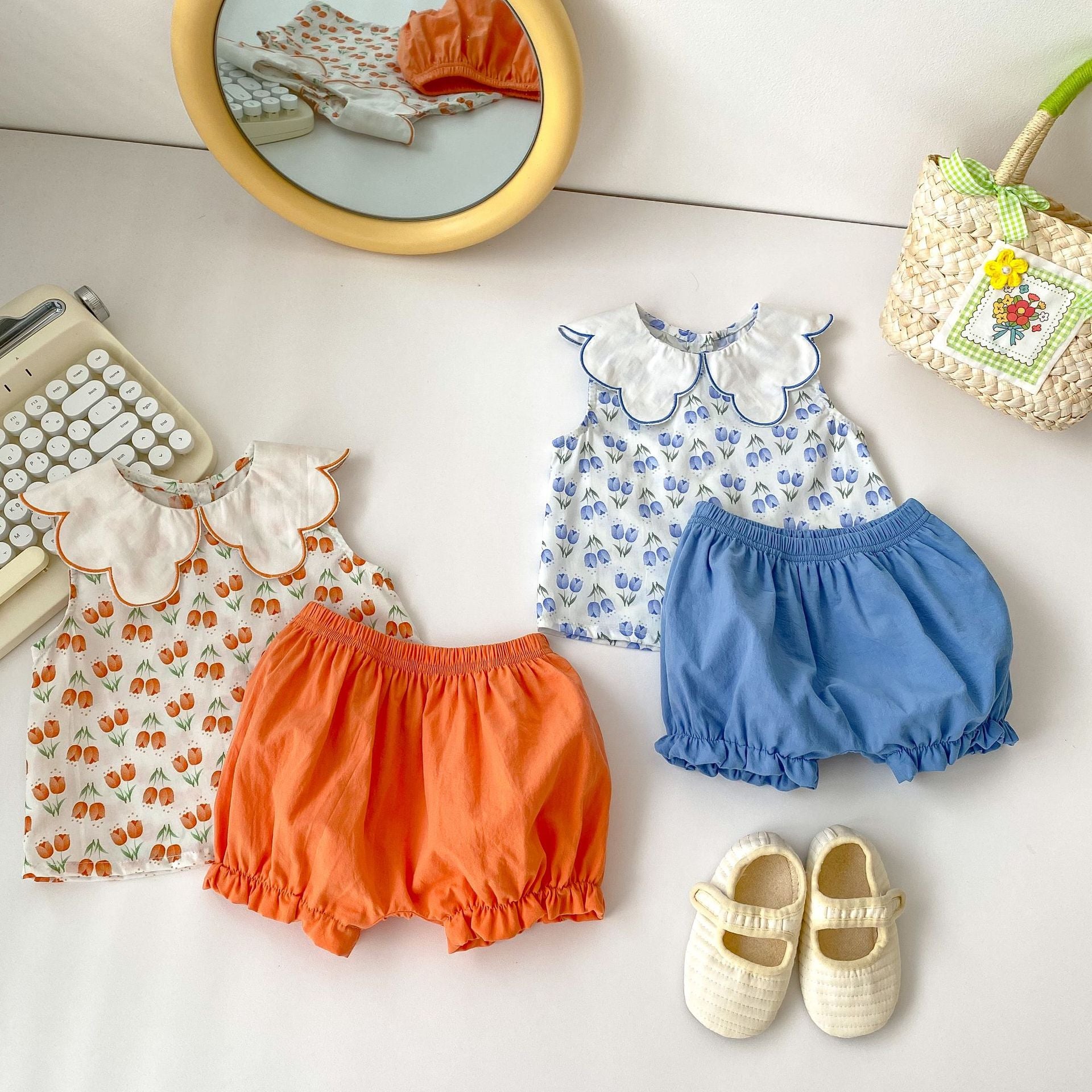 Baby girl wearing a floral pattern ruffle neck shirt and shorts set in blue and orange, perfect for summer.