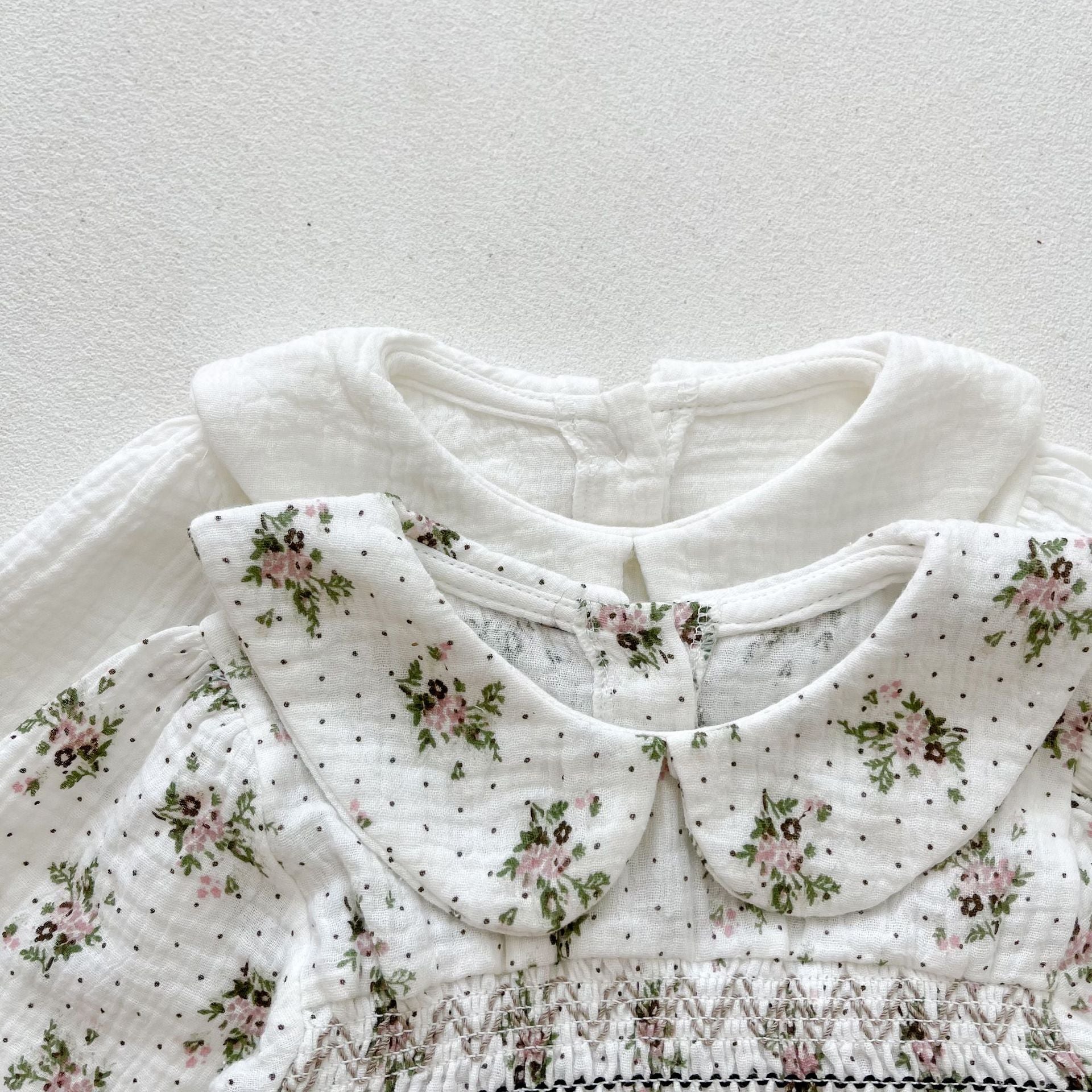 Baby girl wearing a floral print doll collar long-sleeve onesie in white and pink, showcasing a stylish design.