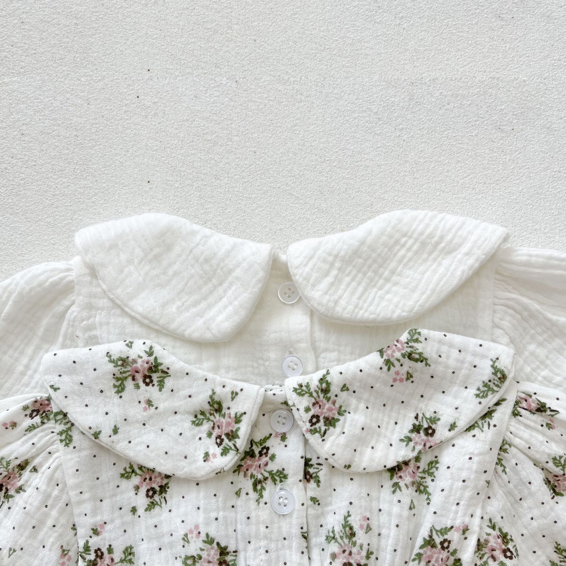 Baby girl wearing a floral print doll collar long-sleeve onesie in white and pink, showcasing a stylish design.