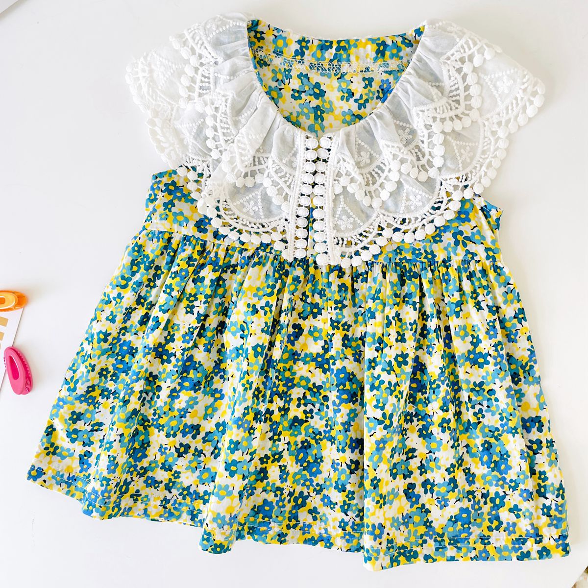 A beautiful baby girl wearing a floral print lace patchwork dress with an O-neck design, showcasing vibrant green colors and intricate patterns.