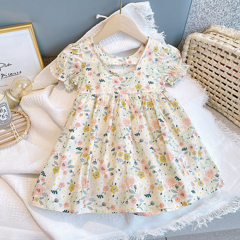 A cute baby girl wearing a floral print O-neck puff-sleeved short dress in apricot color, perfect for summer occasions.