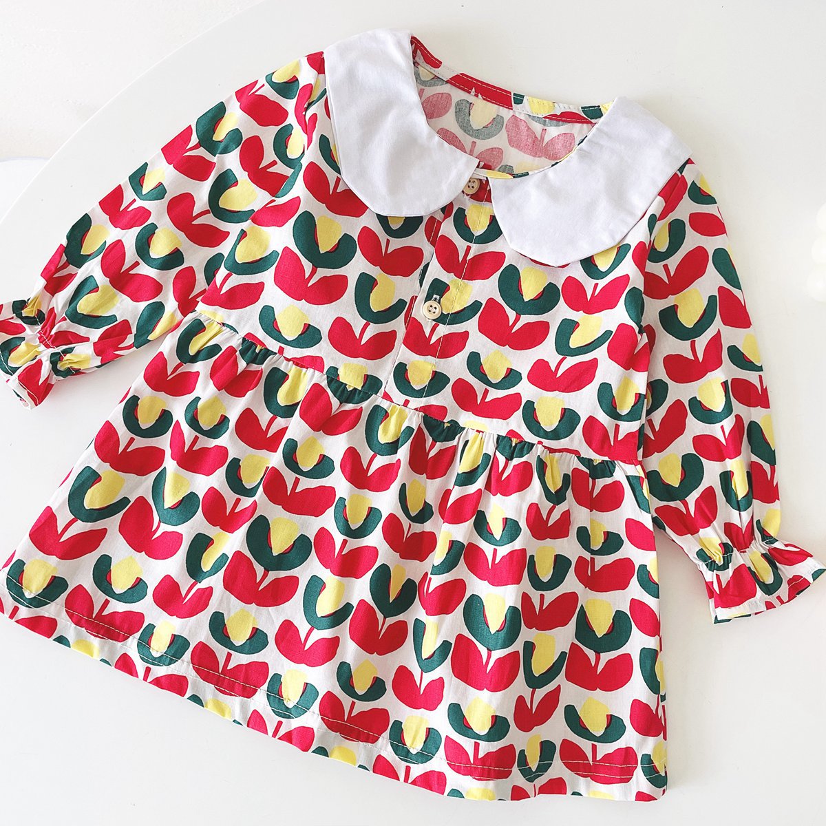 A beautiful baby girl dress featuring a floral print pattern with a doll neck and A-line design, available in red and green colors.