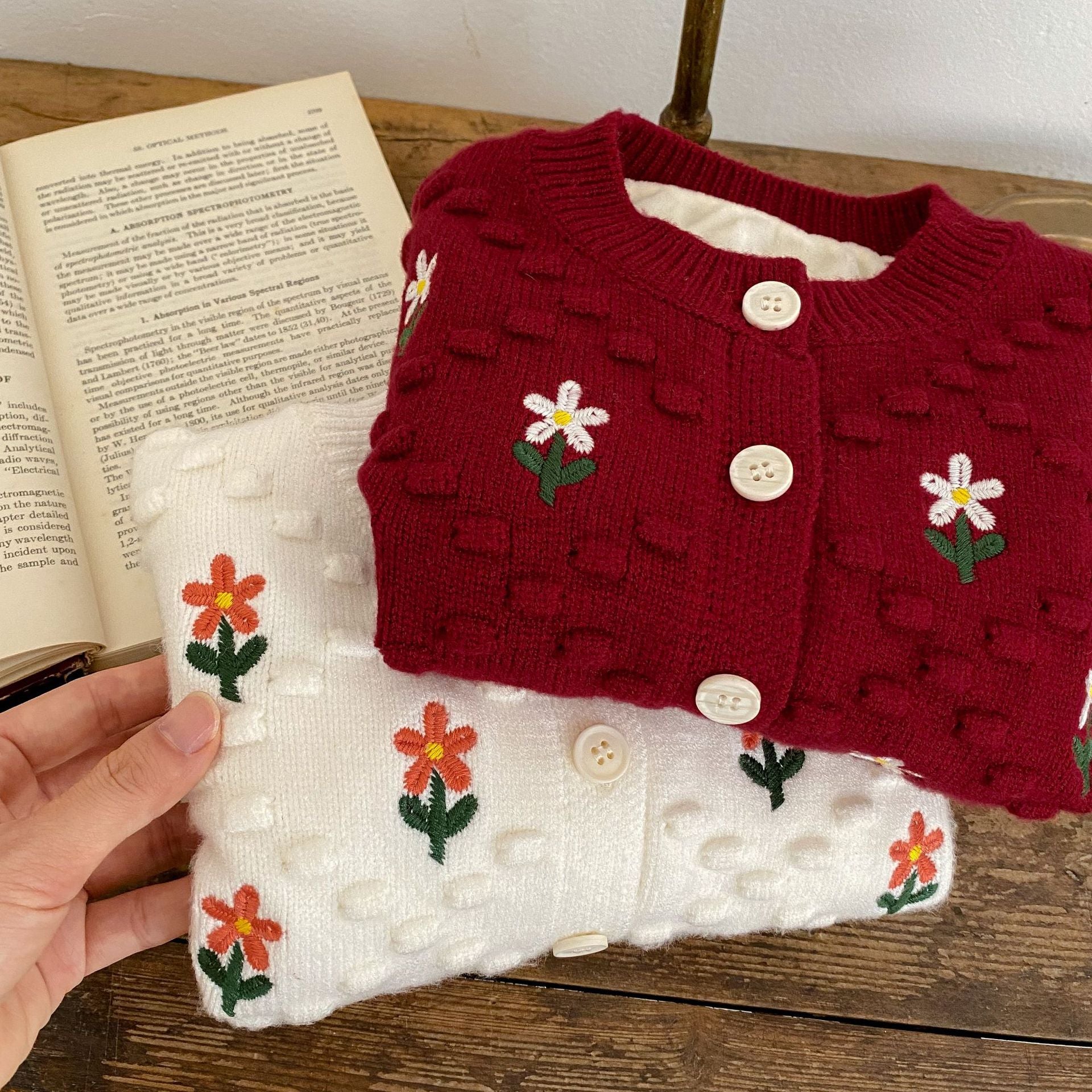 A cozy baby girl cardigan featuring flower embroidery, thickened knit design, available in white and red colors.