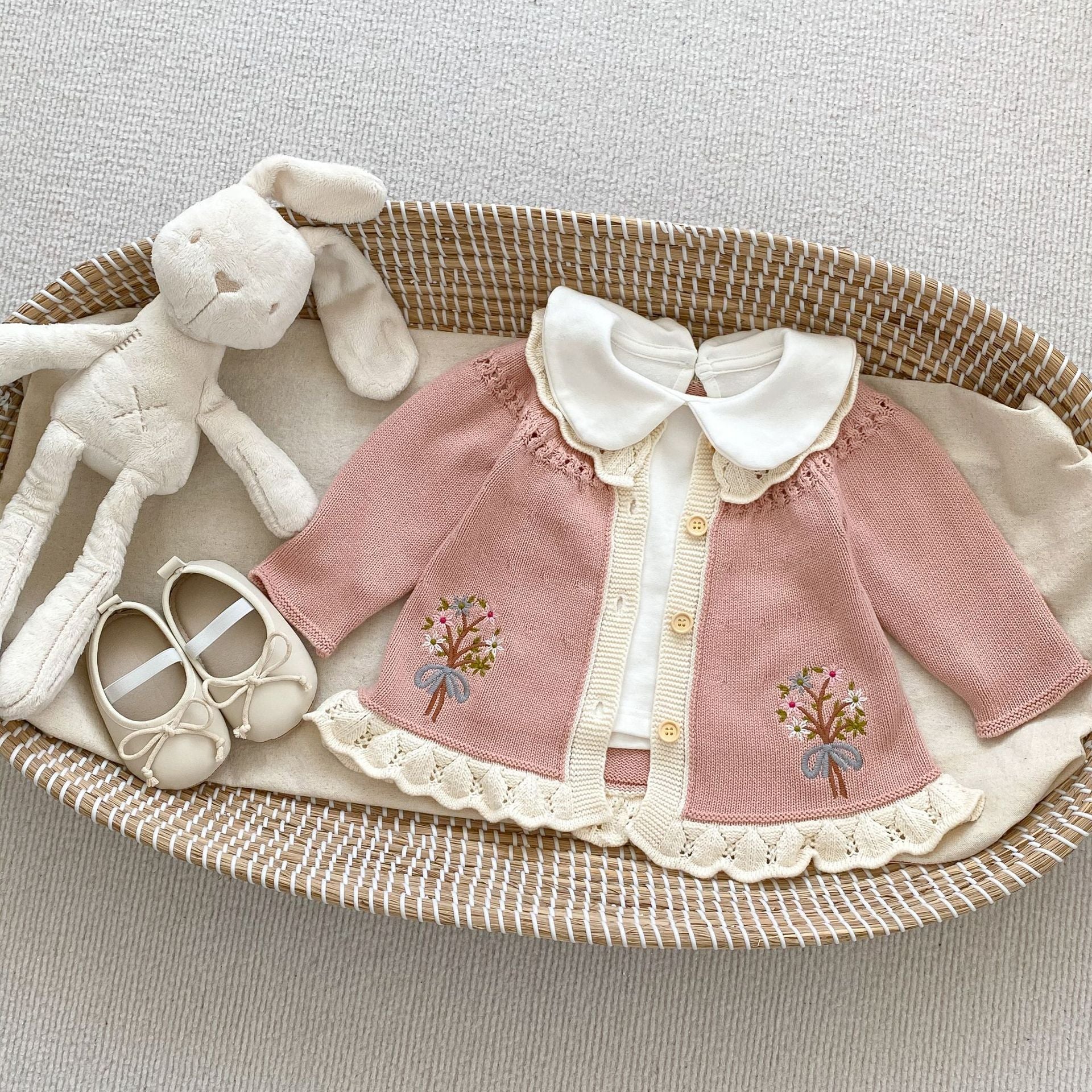 A baby girl wearing a pink embroidered long-sleeved cardigan, showcasing its soft cotton fabric and stylish design.