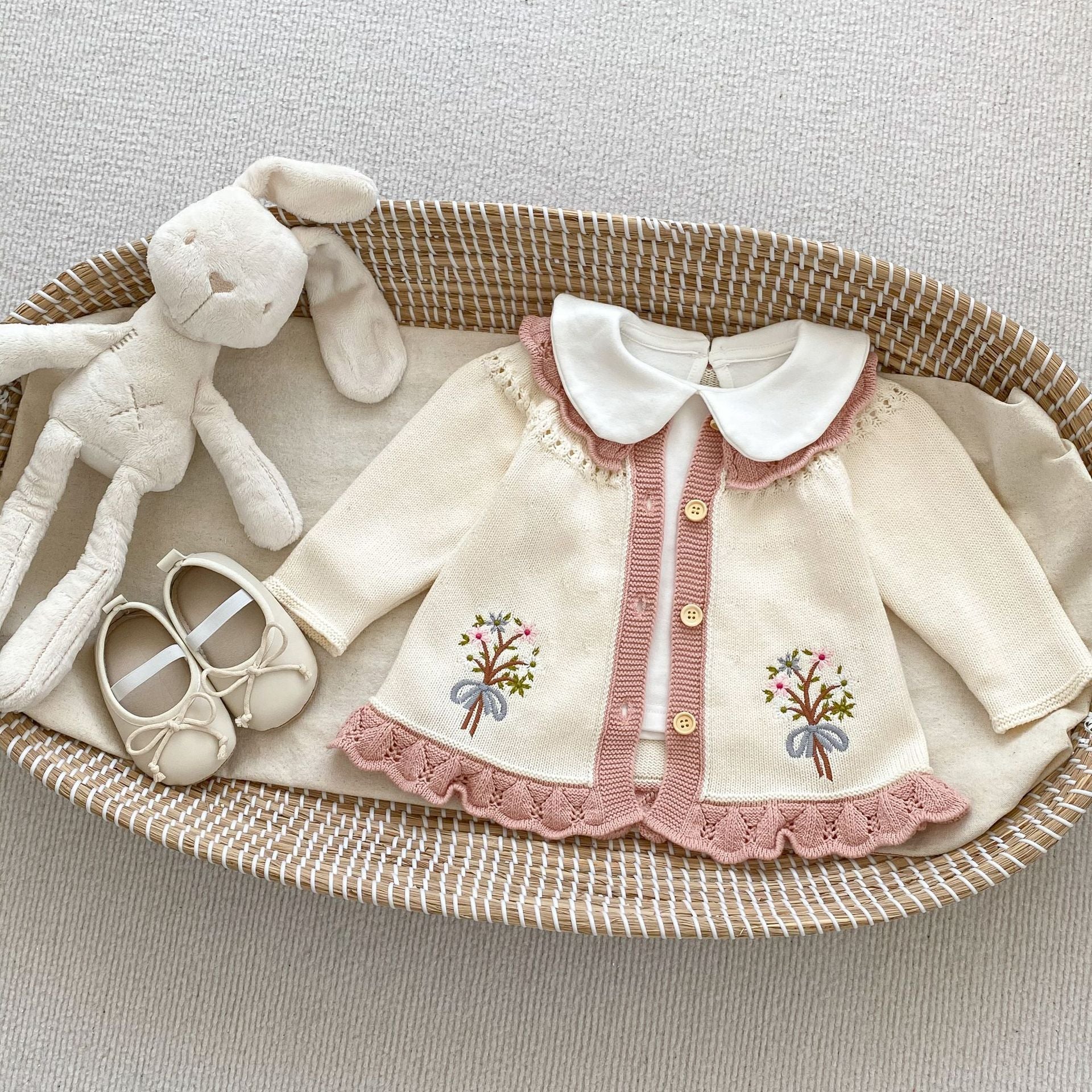 A baby girl wearing a pink embroidered long-sleeved cardigan, showcasing its soft cotton fabric and stylish design.