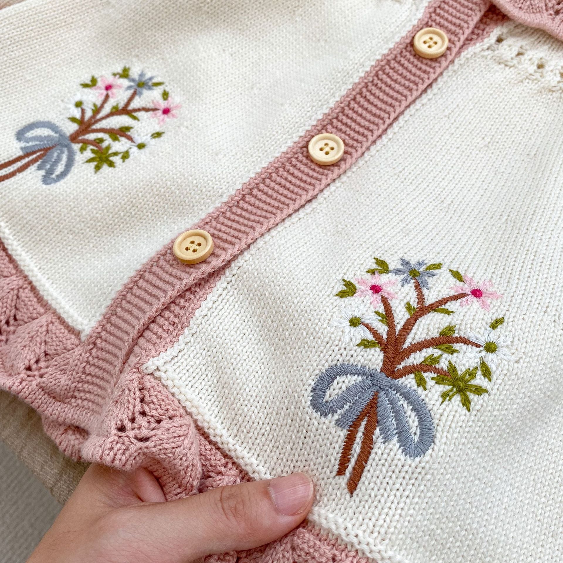 A baby girl wearing a pink embroidered long-sleeved cardigan, showcasing its soft cotton fabric and stylish design.