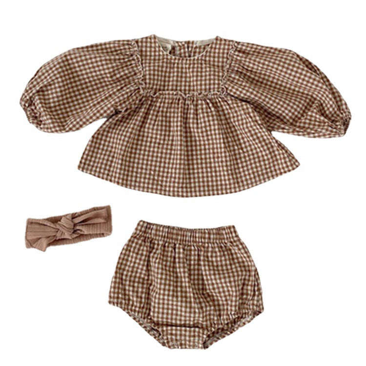 A stylish 3-piece baby girl outfit featuring a plaid pattern blouse, matching shorts, and a headband in apricot and brown colors.