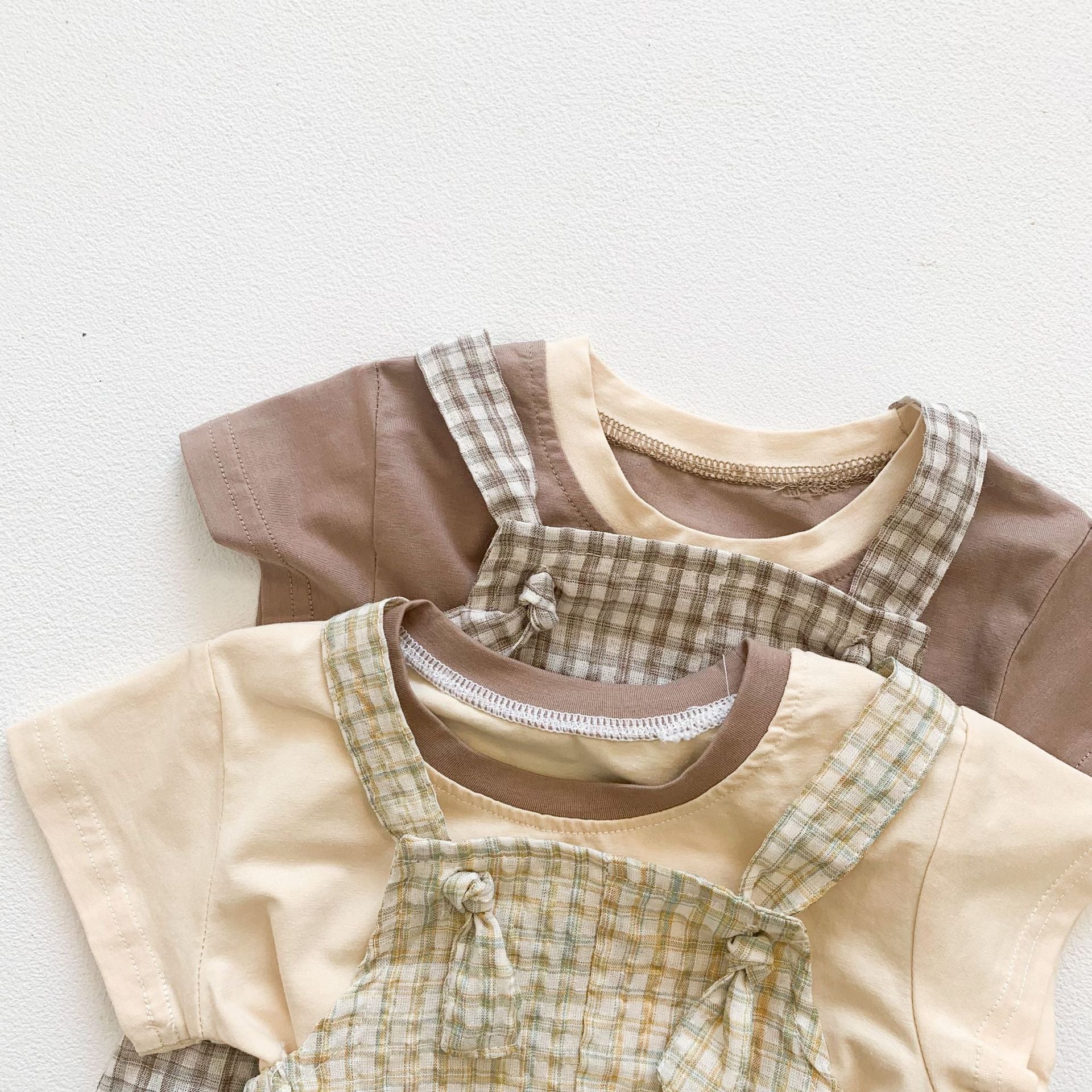 Baby girl wearing a stylish plaid pattern outfit with short sleeves, backpack pants, and a matching hat, perfect for summer.