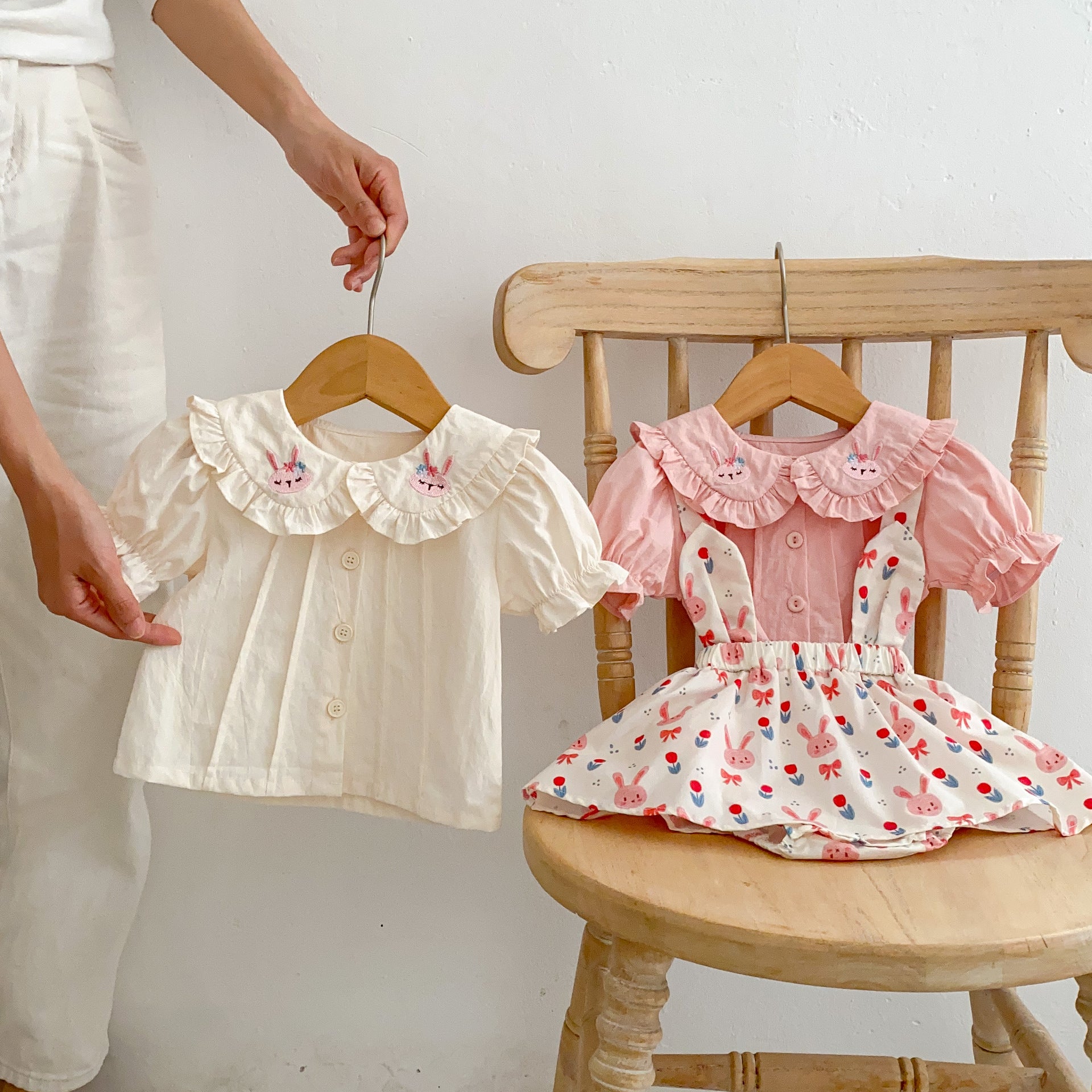 Baby girl wearing a solid color doll neck blouse with a strap dress, showcasing soft cotton fabric in pink and floral patterns.