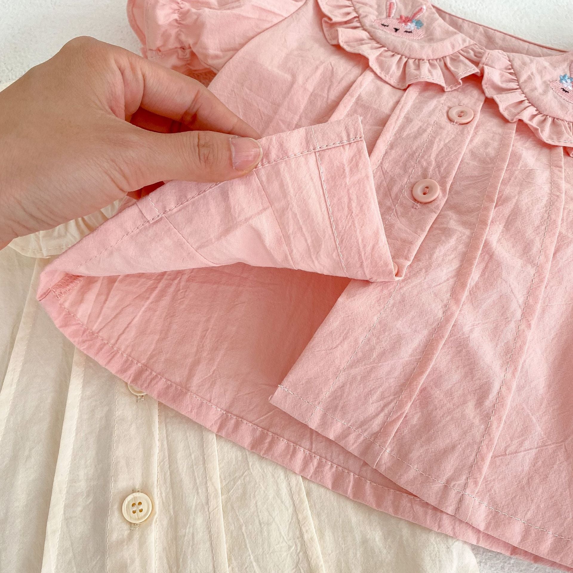 Baby girl wearing a solid color doll neck blouse with a strap dress, showcasing soft cotton fabric in pink and floral patterns.