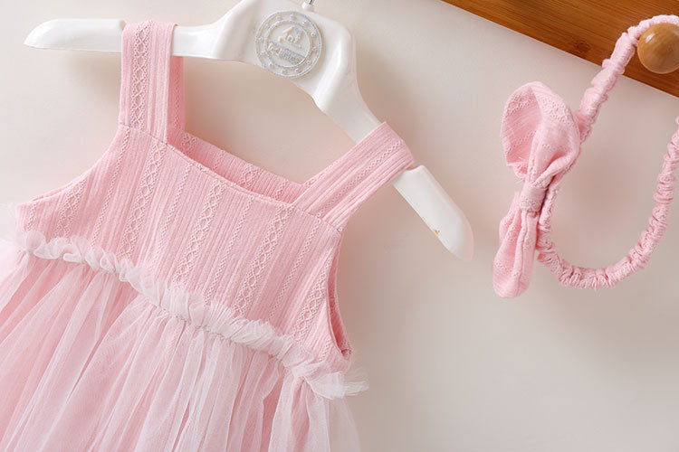 A baby girl wearing a solid color mesh patchwork sleeveless dress in pink, complemented by a delicate headband.