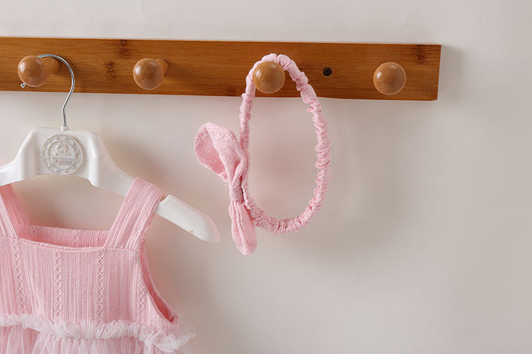 A baby girl wearing a solid color mesh patchwork sleeveless dress in pink, complemented by a delicate headband.