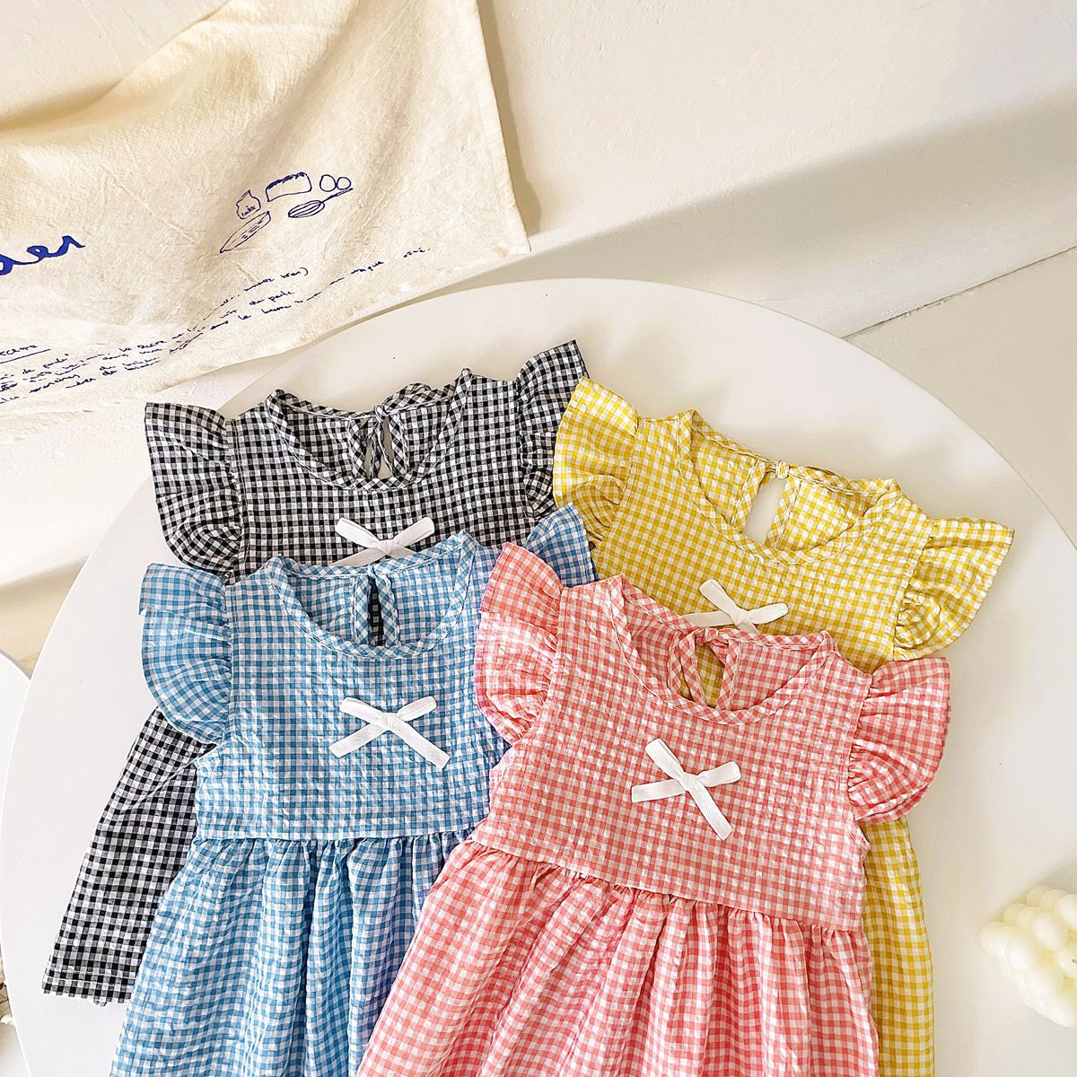 A variety of baby girl summer dresses in floral and plaid patterns, showcasing vibrant colors like pink, blue, and yellow.