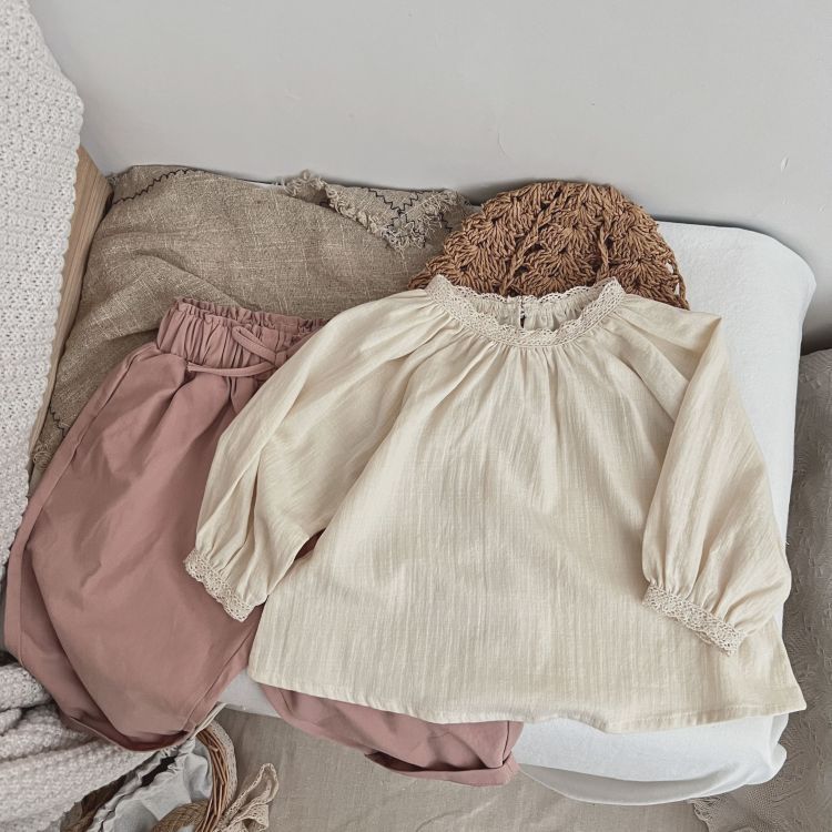 Baby girl wearing a beige long-sleeved top with lace patchwork design, showcasing comfort and style.