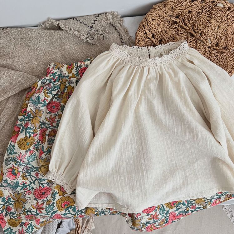 Baby girl wearing a beige long-sleeved top with lace patchwork design, showcasing comfort and style.