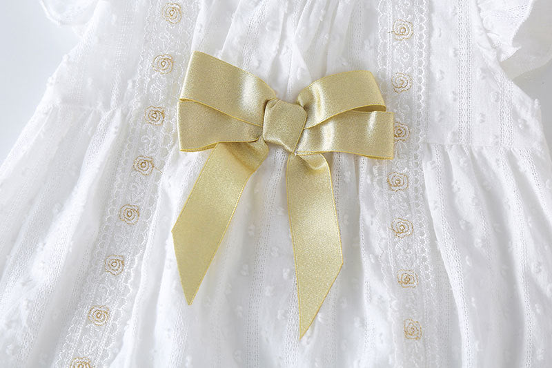 Baby girl wearing a solid white onesie with a gold bow tie patch, perfect for summer outings.