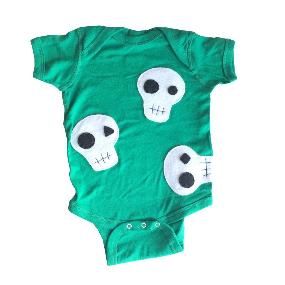 A handmade baby onesie featuring a cute skull design, crafted from soft fabric with appliquéd felt pieces, perfect for infants.