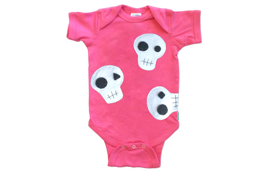 A handmade baby onesie featuring a cute skull design, crafted from soft fabric with appliquéd felt pieces, perfect for infants.