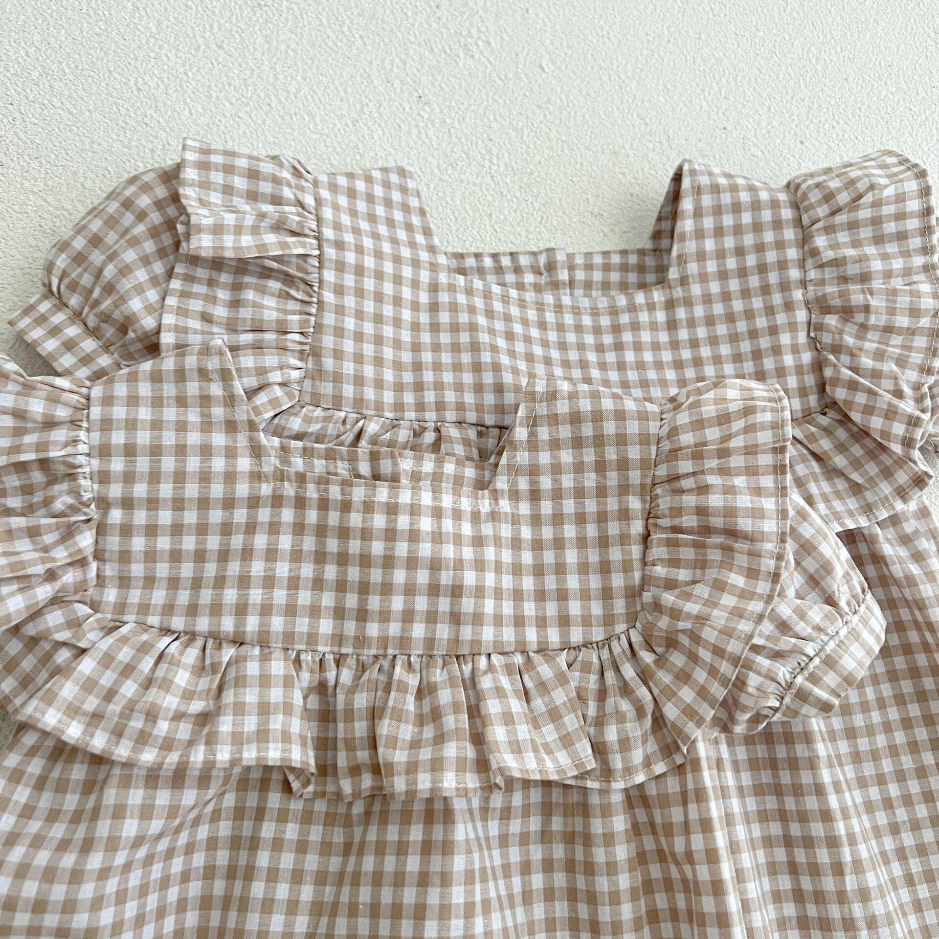 Baby girl wearing a plaid pattern square neck puff sleeves onesie and dress in blue, showcasing a stylish summer outfit.