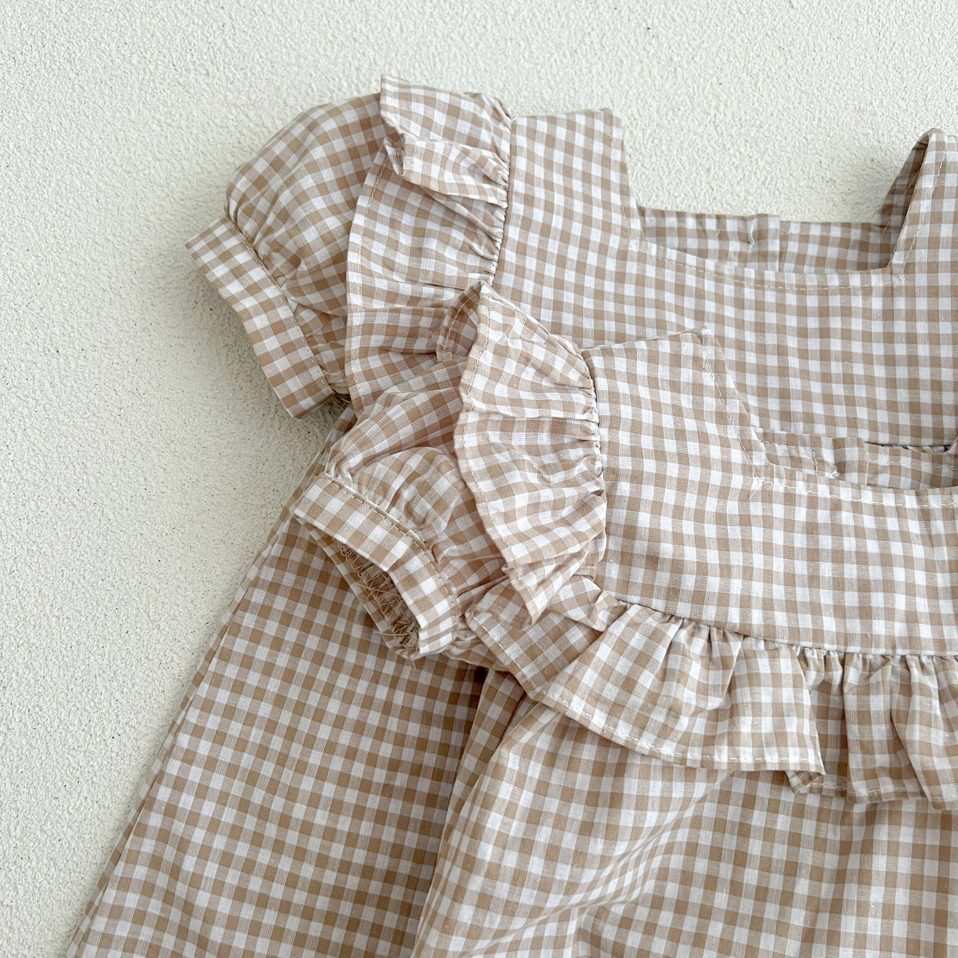 Baby girl wearing a plaid pattern square neck puff sleeves onesie and dress in blue, showcasing a stylish summer outfit.