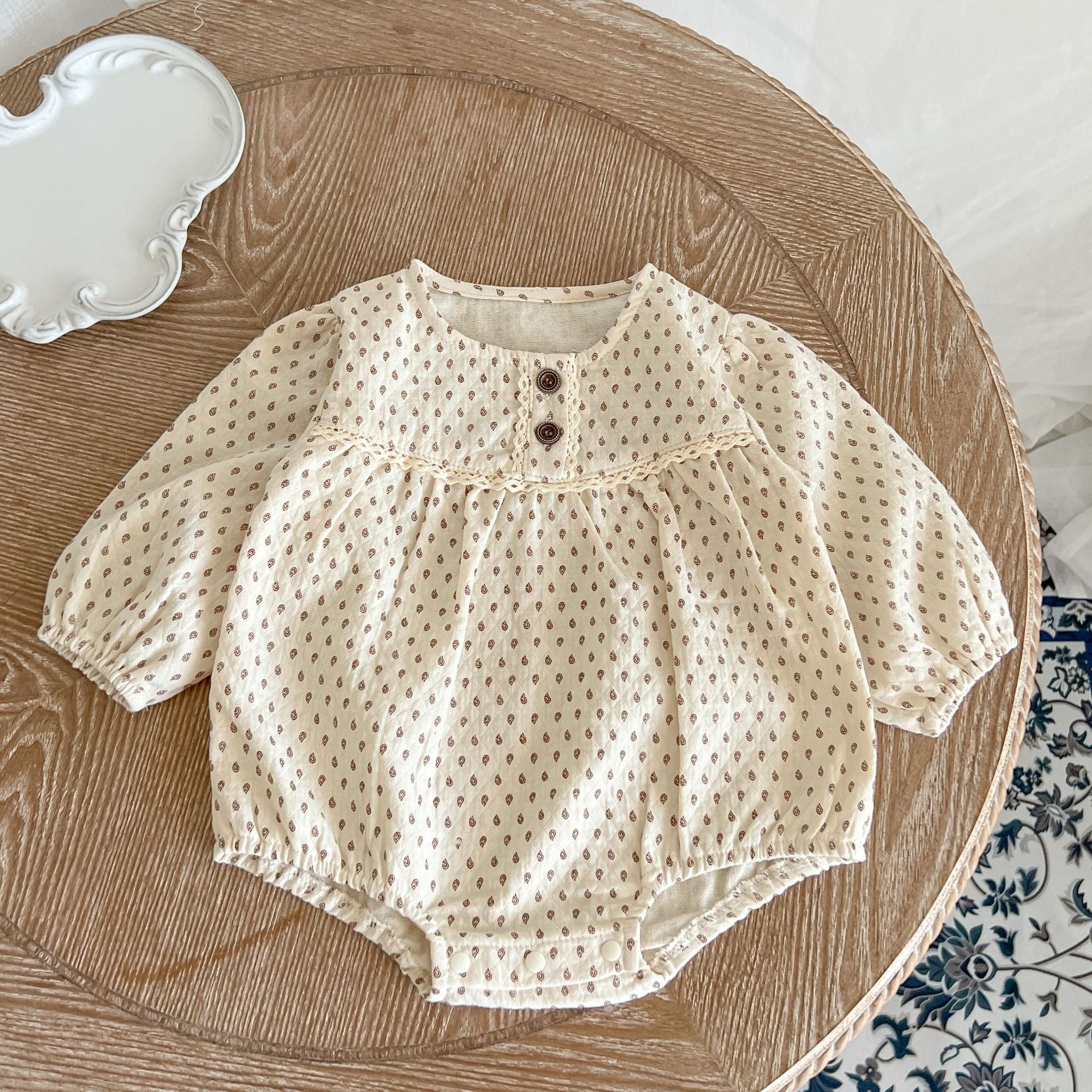 Baby girl wearing a polka dot pattern long sleeve lace design onesie in apricot color, showcasing its stylish and comfortable design.