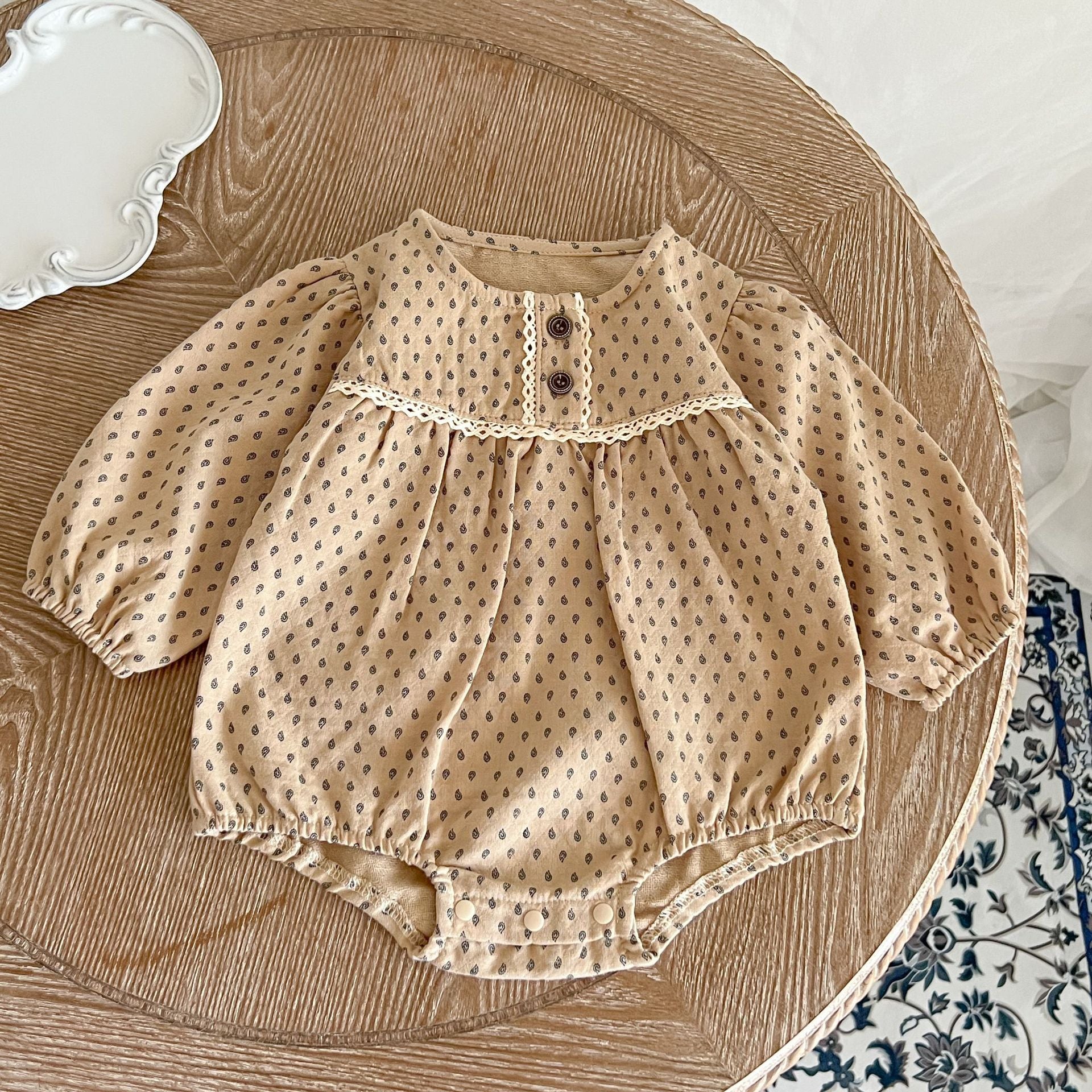 Baby girl wearing a polka dot pattern long sleeve lace design onesie in apricot color, showcasing its stylish and comfortable design.