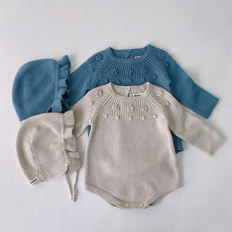 Baby girl wearing a solid color knit onesie with flower patch design in blue and apricot, showcasing comfort and style.