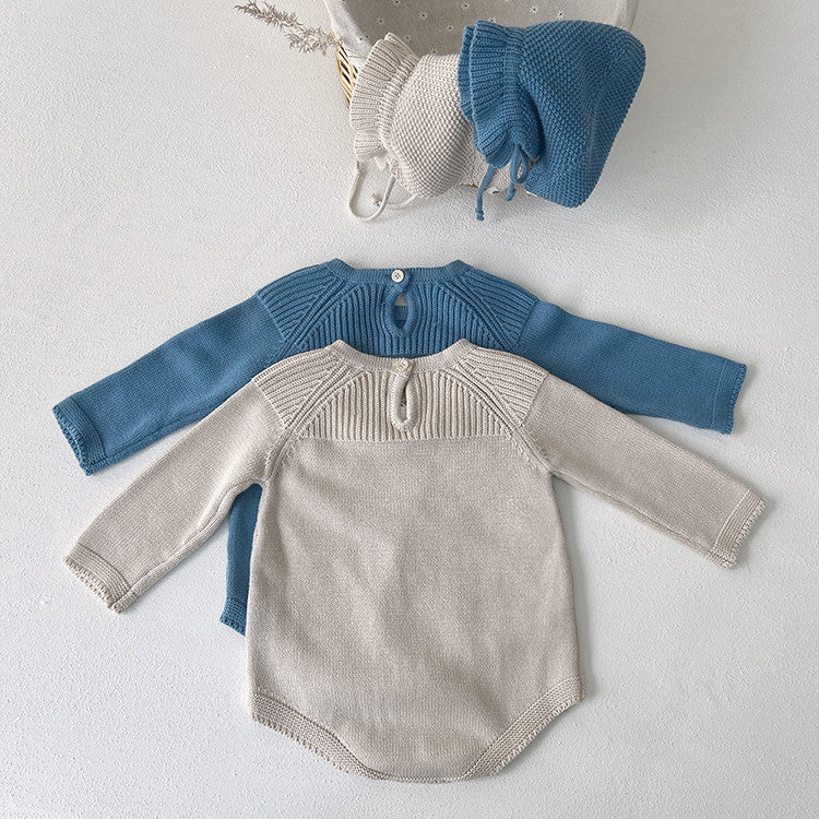 Baby girl wearing a solid color knit onesie with flower patch design in blue and apricot, showcasing comfort and style.