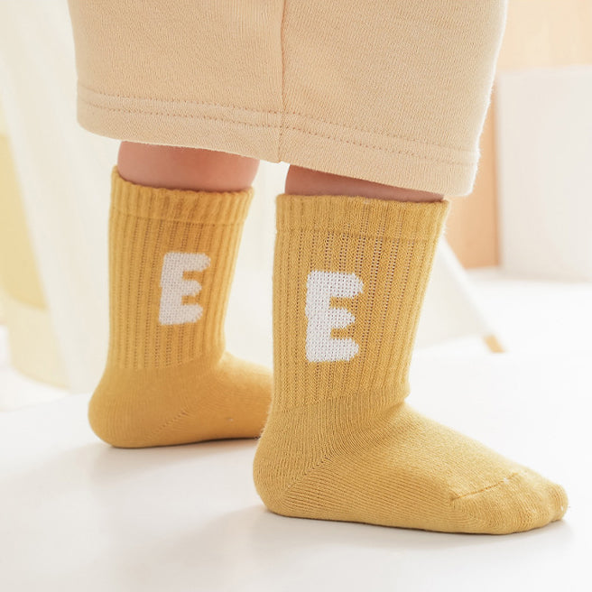 A colorful set of five pairs of baby socks in red, navy blue, blue, yellow, and grey, featuring fun patterns like stripes and cartoons.