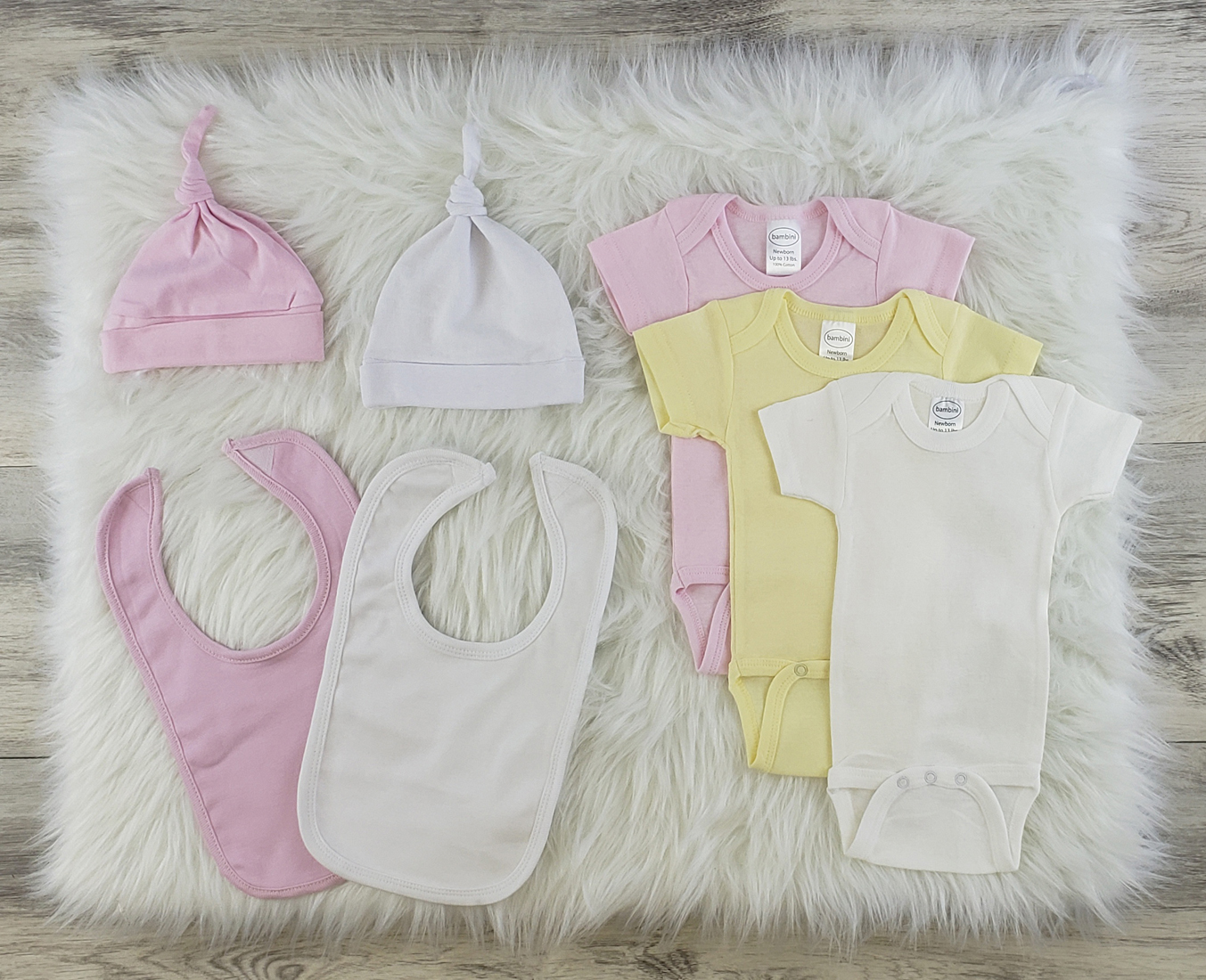 Bambini 7 Pc Layette Baby Clothes Set featuring soft cotton onesies, knotted caps, and bibs in pastel colors, perfect for newborns.