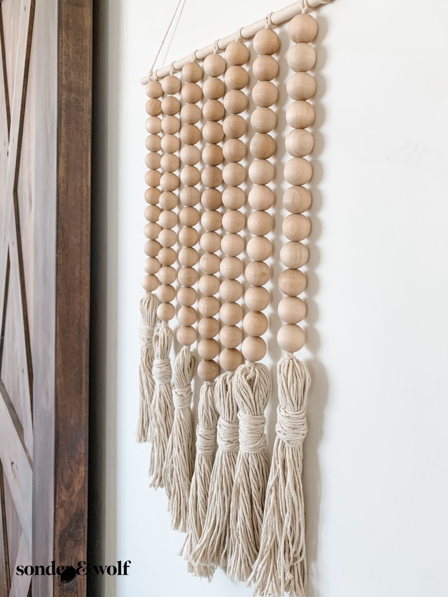 Beaded Wall Art featuring wooden beads and cotton tassels, showcasing a boho-inspired design perfect for home decor.