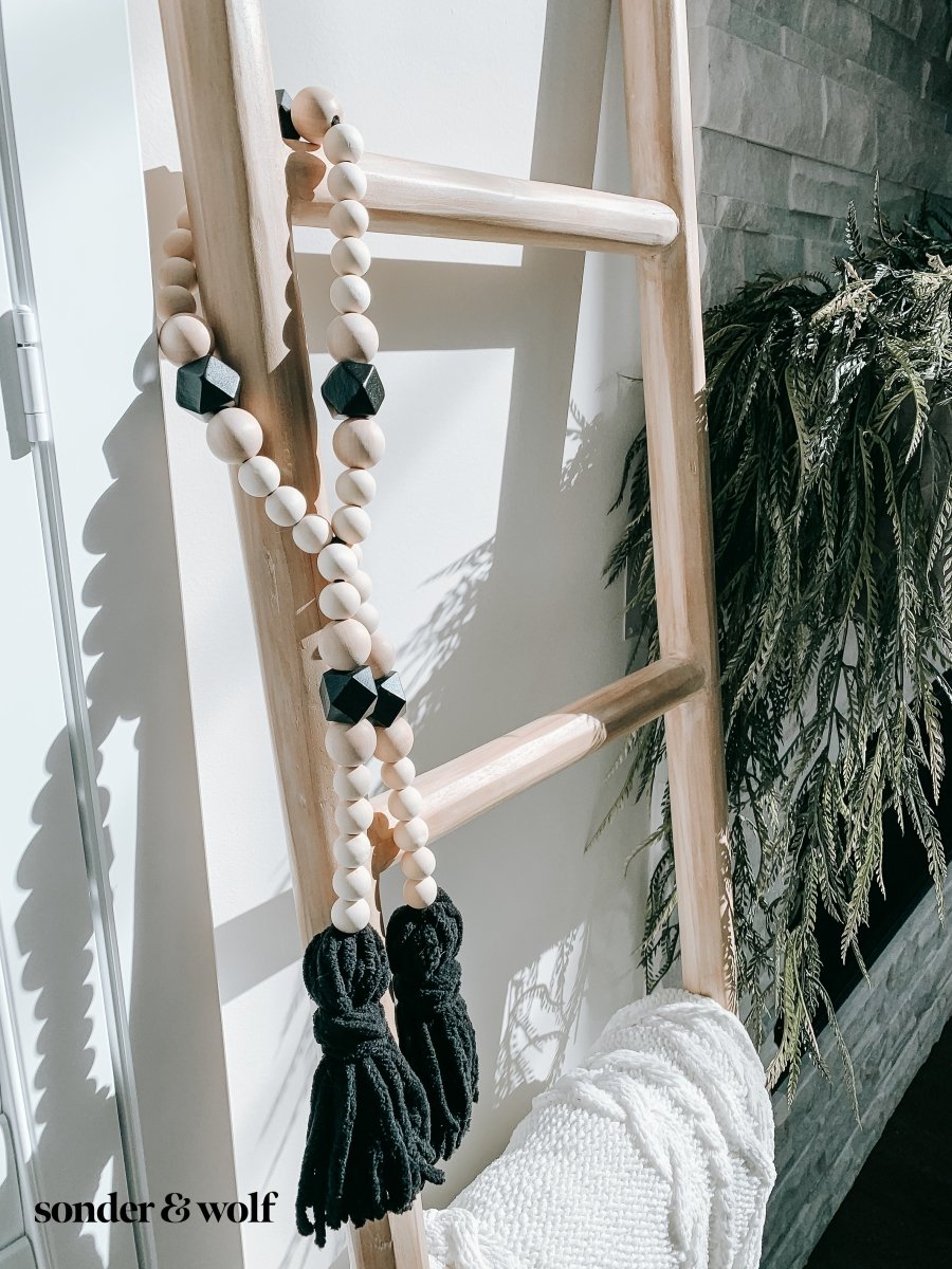 A beautifully handcrafted Boho Wood Bead Garland featuring light unfinished wood beads and stylish black tassels, perfect for home decor.