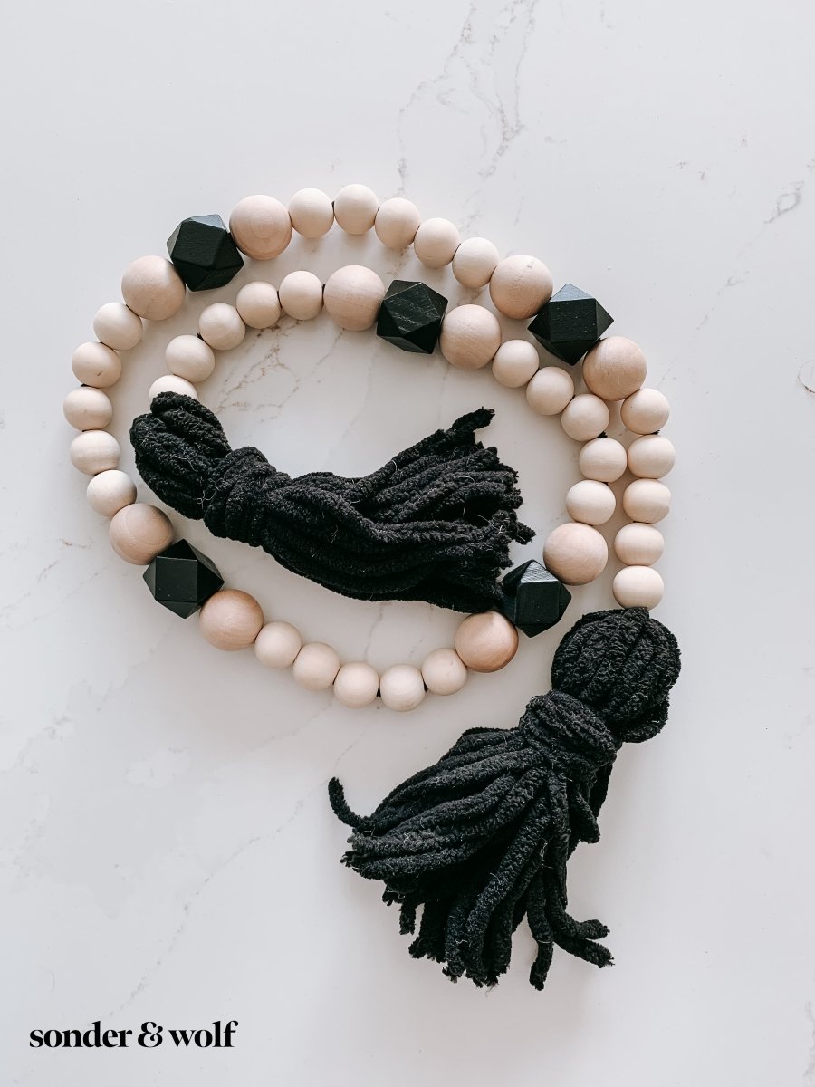 A beautifully handcrafted Boho Wood Bead Garland featuring light unfinished wood beads and stylish black tassels, perfect for home decor.