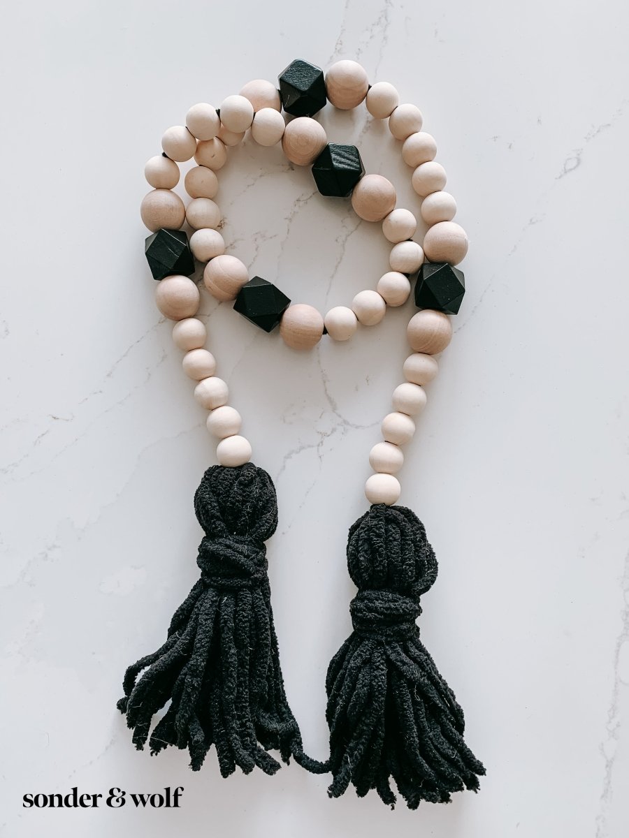 A beautifully handcrafted Boho Wood Bead Garland featuring light unfinished wood beads and stylish black tassels, perfect for home decor.