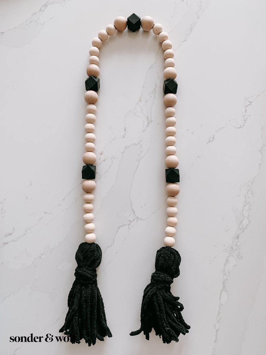 A beautifully handcrafted Boho Wood Bead Garland featuring light unfinished wood beads and stylish black tassels, perfect for home decor.