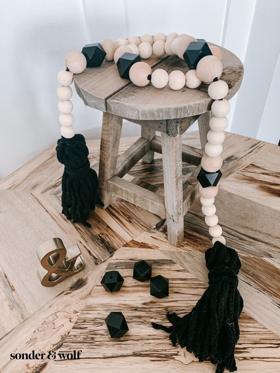 A beautifully handcrafted Boho Wood Bead Garland featuring light unfinished wood beads and stylish black tassels, perfect for home decor.