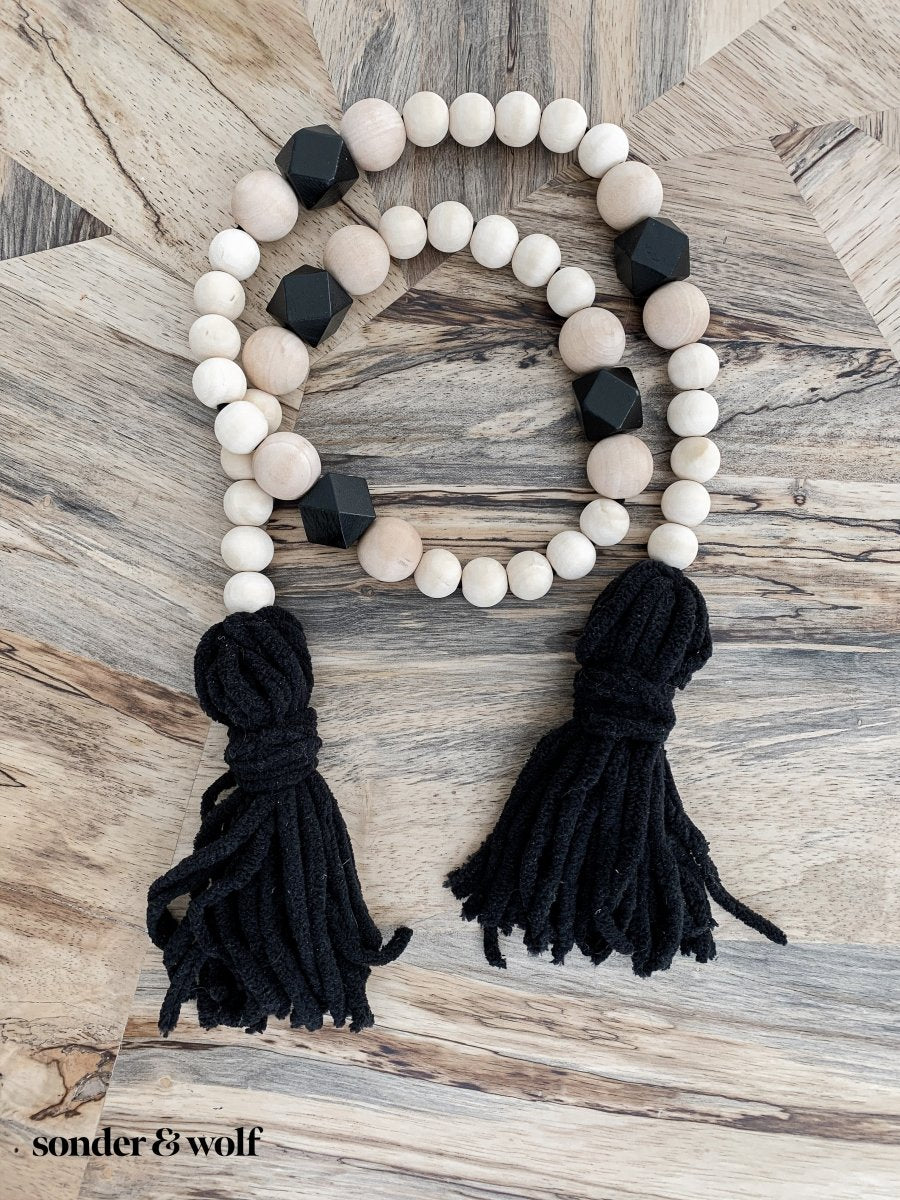 A beautifully handcrafted Boho Wood Bead Garland featuring light unfinished wood beads and stylish black tassels, perfect for home decor.