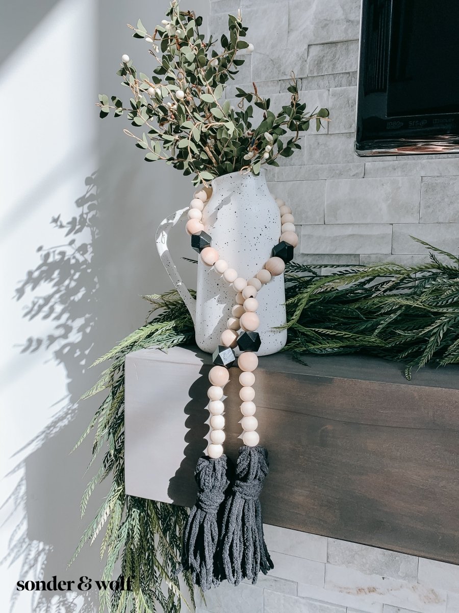 A beautifully handcrafted Boho Wood Bead Garland featuring light unfinished wood beads and stylish black tassels, perfect for home decor.