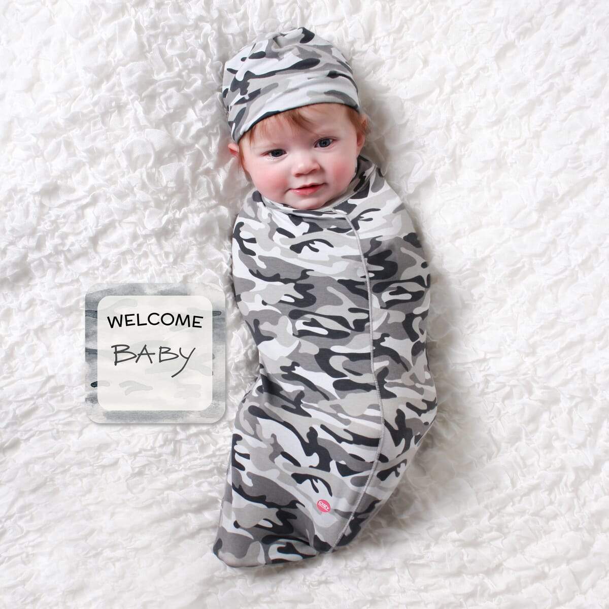 Camo Baby cocoon swaddle set featuring soft fabric, matching headpiece, and newborn announcement card, perfect for cozy moments.