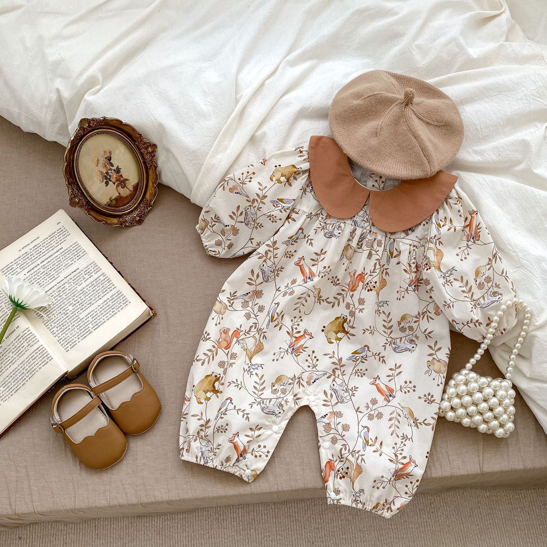 A cute baby girl wearing a Cartoon Graphic Autumn Romper in white with floral patterns, perfect for autumn fashion.