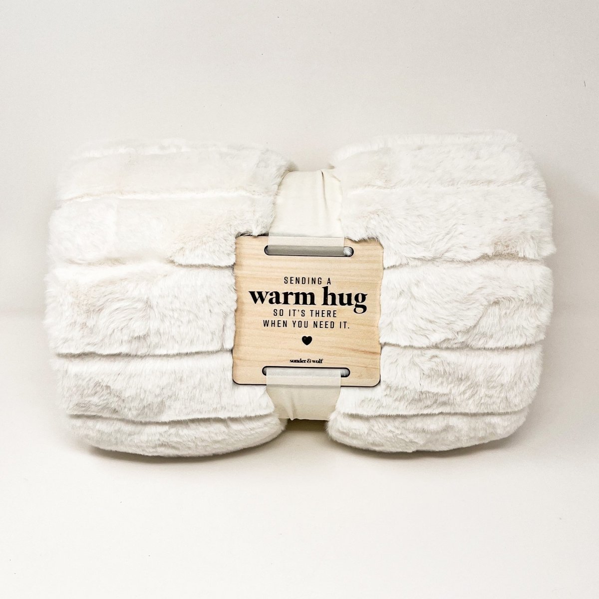 A cozy faux fur blanket with a wooden tag that reads 'With Warm Hug', perfect for providing comfort and warmth.