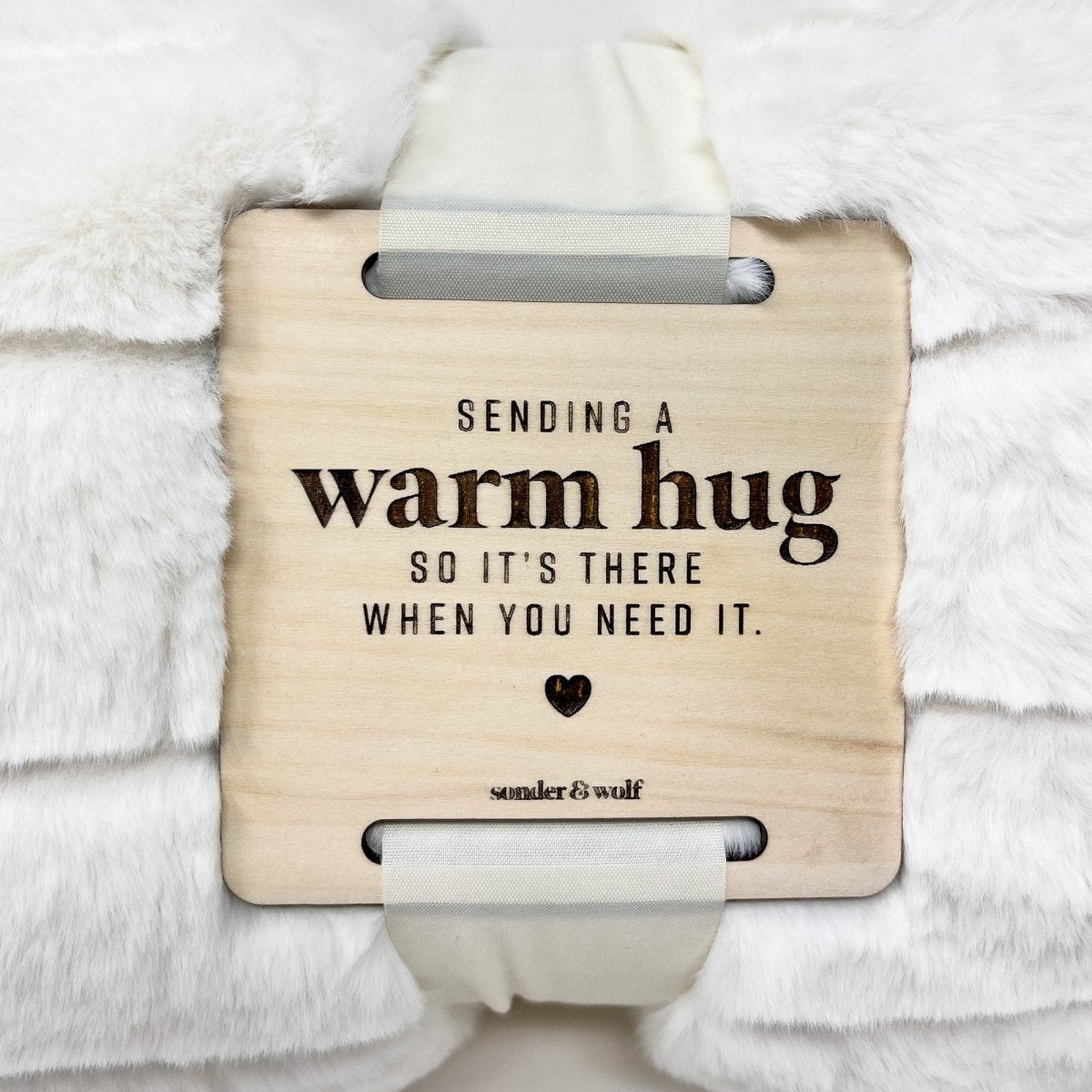 A cozy faux fur blanket with a wooden tag that reads 'With Warm Hug', perfect for providing comfort and warmth.