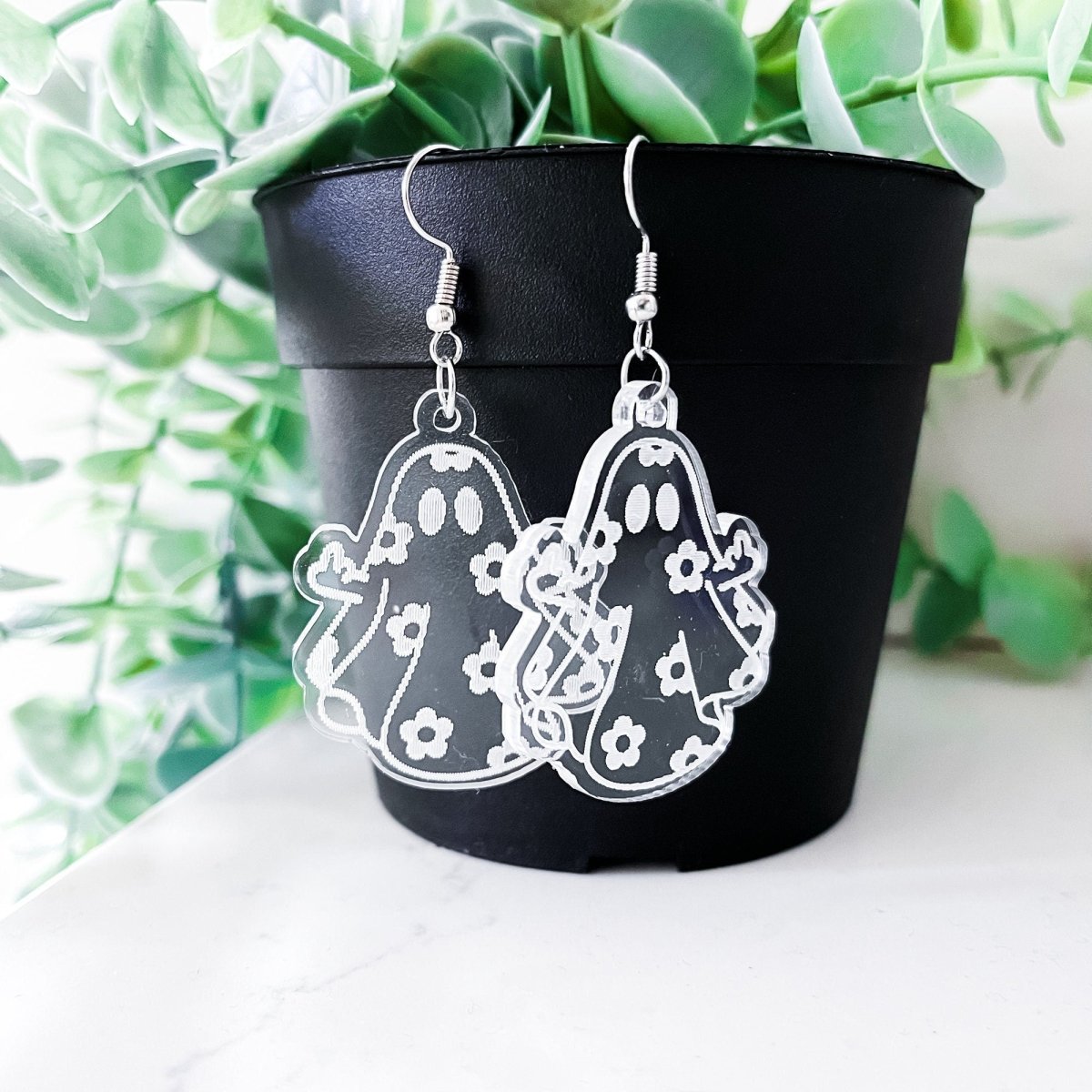 A pair of acrylic ghost dangle earrings featuring a laser-engraved daisy ghost design, perfect for adding a spooky touch to any outfit.