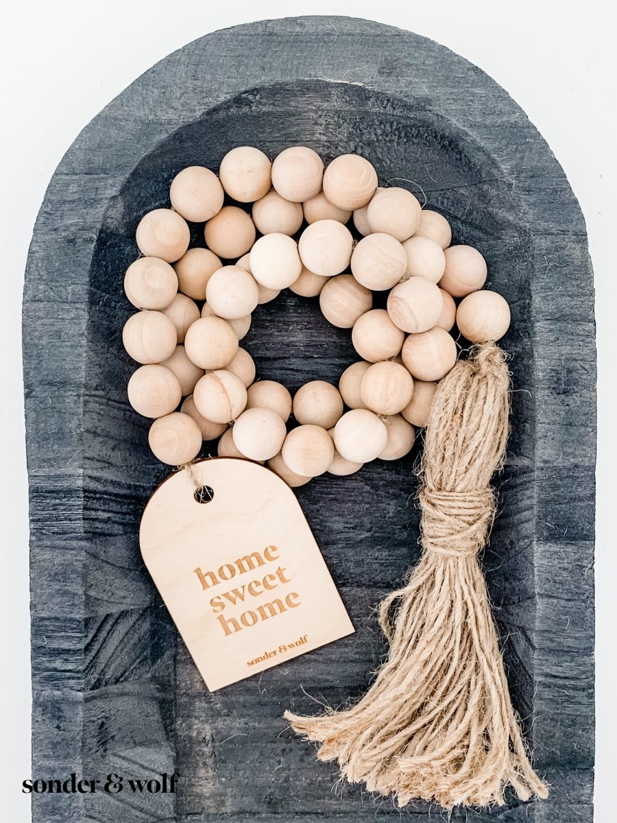 Home Sweet Home Garland featuring natural wood beads and a jute tassel, perfect for home decor.