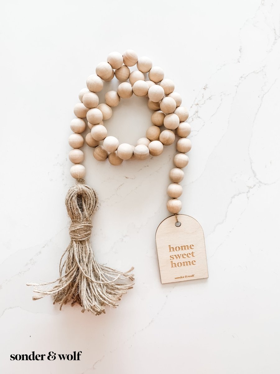 Home Sweet Home Garland featuring natural wood beads and a jute tassel, perfect for home decor.