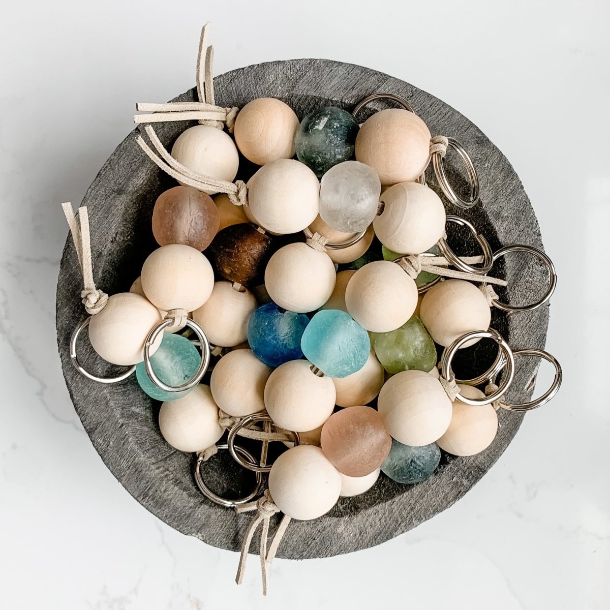 A colorful Sea Glass Bead Keychain featuring recycled glass beads and natural wood beads, attached to a leather string keyring.