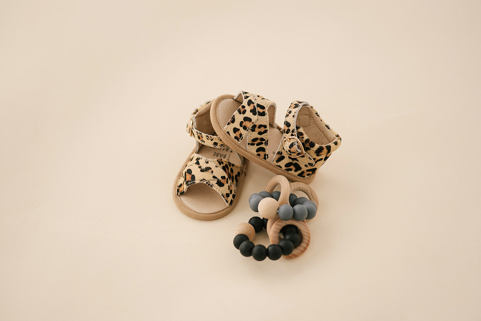 A pair of stylish leopard print baby sandals made of soft leather, featuring rubber treads for safety and comfort.